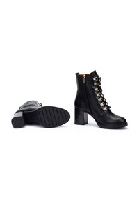 Botas de tobillo de cuero negro con un alto tacón cuadrado, cordones en la parte delantera y detalles de hardware en dorado. Cuentan con una cremallera lateral y una suela texturizada.