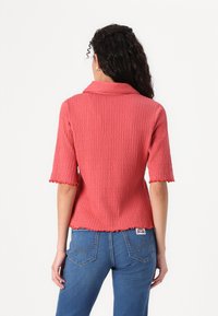 Geribbelde, koraalkleurige top met korte mouwen, een kraag en geschulpte randen, gecombineerd met hoog-taille blauwe jeans met achterzakken en stikdetails.