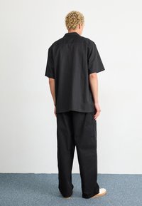 Czarna koszula krótki rękaw i luźne spodnie wykonane z lekkiego materiału, z luźnym krojem i subtelnymi detalami szwów. Białe buty dopełniają stylizację.