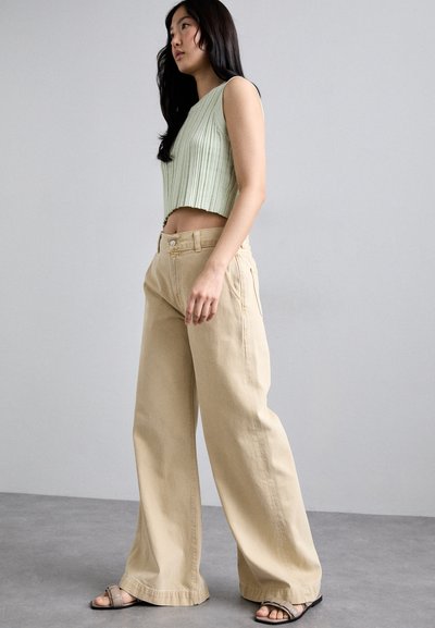 Un crop top côtelé vert clair associé à un pantalon large beige. Les deux vêtements sont fabriqués dans un tissu doux, offrant une coupe naturelle et ample.