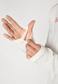 Vit långärmad skjorta med ett stort manschettöppning. Tyget ser slätt, elastiskt och åtsittande ut, med en subtil textur och sydda sömmar.