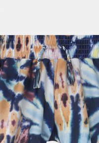 Calções de banho tie-dye com um padrão de cores azul, laranja e creme. Apresenta uma cintura franzida com laços ajustáveis e tecido texturizado.