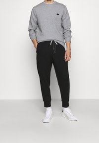 Grå crewneck-tröja med en liten logotyp, kombinerad med svarta smala träningsbyxor med dragsko och vita sneakers.