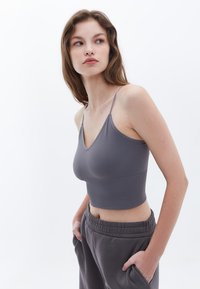 Camiseta de cropped gris con ribetes, tirantes finos y diseño de escote en V, combinada con pantalones de chándal grises con cintura elástica y bolsillos laterales.