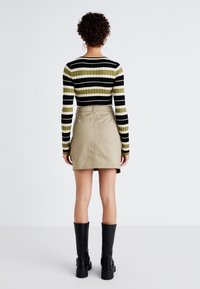 Pruhovaný žebrovaný svetr v černé, olivové a bílé barvě; béžová minisukně s kapsami; černé kozačky po kolena s masivní podrážkou.