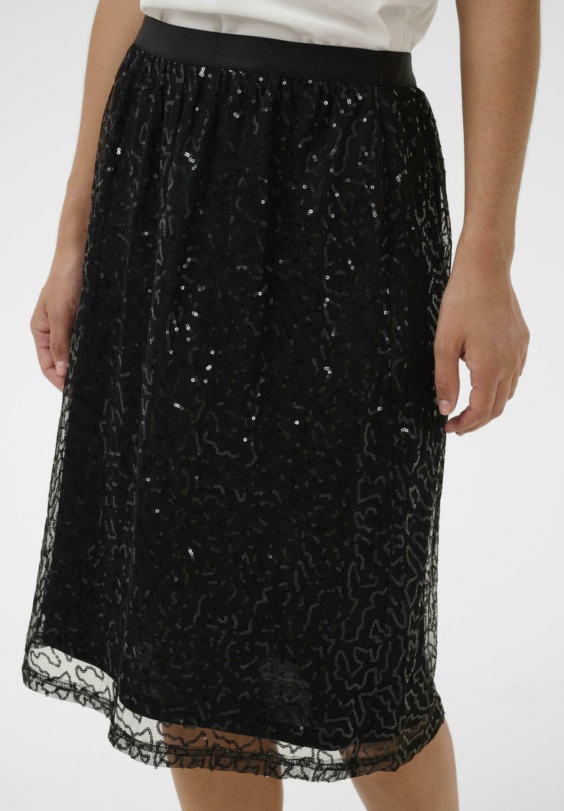 Jupe noire en tissu transparent avec un motif texturé et des paillettes disséminées. Présente une taille noire simple et une coupe au genou.