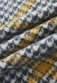 Woolen fabric featuring a houndstooth pattern in navy, white, and mustard yellow, with a soft texture and visible fibers.