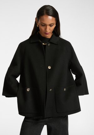 Cappotto nero in lana con vestibilità rilassata, chiusura a bottoni, due tasche frontali e bottoni metallici. Il colletto alto e le maniche lunghe creano una silhouette ben definita.