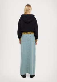 Felpa nera corta con cappuccio, abbinata a una lunga gonna di jeans azzurri chiari con tasche e taglio dritto. Scarpe con plateau nere.