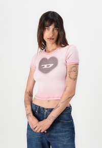 Pink cropped t-shirt made of ribbed fabric with short sleeves; features a gray heart design and logo in the center, outlined in darker pink.