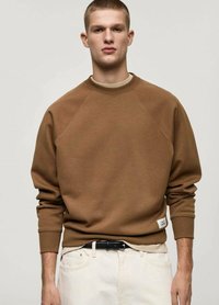 Bruine sweatshirt met een ronde hals, raglanmouwen en geribbelde manchetten. Draag het over een lichtgekleurde shirt, gecombineerd met lichte broek en een zwarte riem.