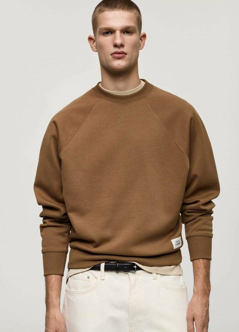 Bruine sweatshirt met een ronde hals, raglanmouwen en geribbelde manchetten. Draag het over een lichtgekleurde shirt, gecombineerd met lichte broek en een zwarte riem.