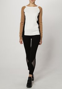 Il maglione presenta un corpo bianco con maniche raglan color cammello e nero, abbinato a leggings neri con inserti in rete sui lati.