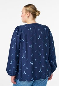 Temno modra bluza z rožnim motivom v svetlo modri barvi; ima napihnjene rokave in okrogel izrez. Mehka, teksturirana tkanina.