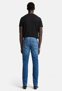 Niebieskie dżinsy o prostym kroju, z dwoma tylkimi kieszeniami i subtelnymi detalami wyszycia, w połączeniu z czarnym t-shirtem z okrągłym dekoltem.