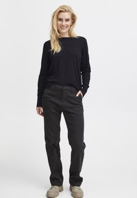 Črn dolg rokav, temno siv hlače, oba izdelana iz mehkega materiala. Hlače imajo žepe in raven kroj. Svetli športni copati.