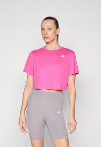 Vaaleanpunainen lyhythihainen cropped-t-paita, jossa valkoinen logo, yhdistettynä harmaisiin korkeavyötäröisiin pyöräilyshortseihin, joissa on yhteensopiva logo ja ompeluyksityiskohdat.
