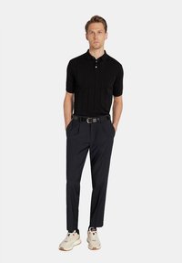 Czarna koszulka polo z krótkim rękawem o ryflowanej fakturze, zestawiona z granatowymi spodniami i białymi butami sportowymi z akcentami. Do zestawu dołączony czarny skórzany pasek.