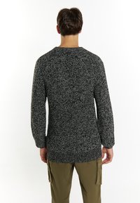 Pulover texturat negru și alb, cu mâneci lungi, guler rotund și o croială lejeră, asortat cu pantaloni cargo de culoare măsline.