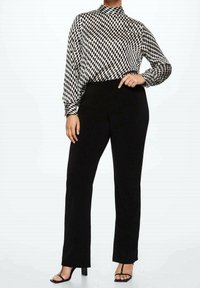 Schwarz-weiße karierte Bluse mit langen Ärmeln und hohem Kragen, kombiniert mit schwarzen eng anliegenden Hosen und schwarzen Riemchensandalen.