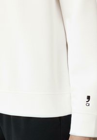 Witte sweatshirt met een gladde textuur, geribbelde manchetten en een zwart logo op de mouw. Zichtbare naaddetails en een relaxte pasvorm.