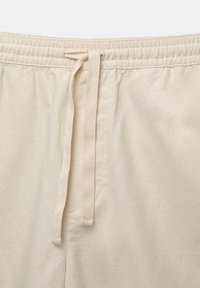 Pantalon en coton beige avec taille élastique et cordon noué à l'avant, montrant la texture du tissu et les détails des coutures.