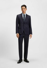 Completo blu con giacca aderente e pantaloni dritti. Abbinato a una camicia a quadri chiari e una cravatta a fantasia. Tessuto morbido e scarpe eleganti.