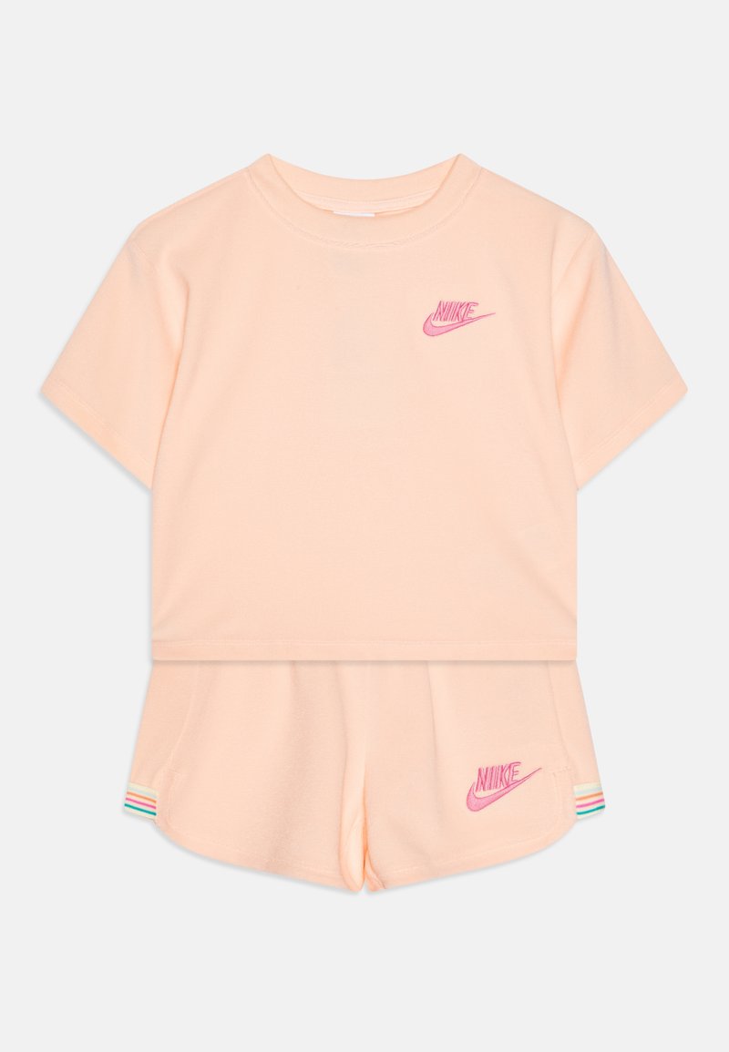 Σετ από βαμβάκι σε ροδακινί χρώμα, αποτελούμενο από κοντομάνικη μπλούζα και κοντές σορτς. Διαθέτει κεντημένο ροζ λογότυπο Nike και πολύχρωμες ρίγες ως λεπτομέρειες.