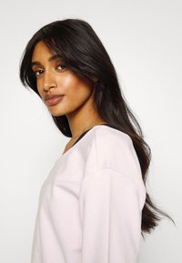 Sweatshirt rosa claro com um corte descontraído, apresentando um design liso, decote amplo e detalhes pretos no decote. Textura suave.