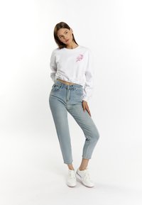 Witte cropped sweatshirt met roze borduursels, gecombineerd met lichtblauwe high-waisted jeans en witte sneakers. Eenvoudig ontwerp, relaxte pasvorm.