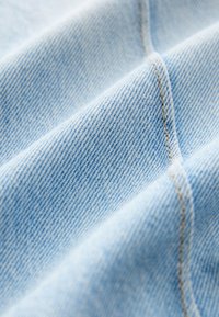 Tessuto di denim azzurro chiaro con una consistenza morbida, caratterizzato da una sottile trama diagonale e cuciture a contrasto color cuoio lungo le cuciture.