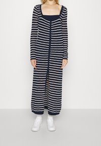 Dlouhý cardigan v námořnické modré a bílé pruhy vyrobený z lehkého pleteného materiálu, s čtvercovým výstřihem a knoflíky vpředu.