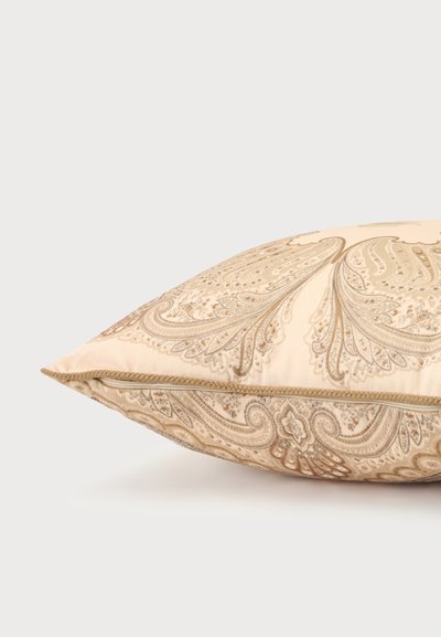 Coussin beige avec motifs paisley complexes dans des tons or atténués et brun clair, avec fermeture éclair latérale.