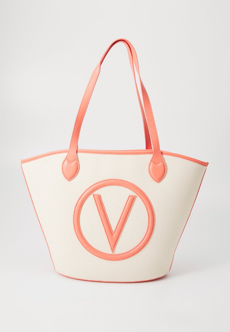 Canvas tote bag met koraal leren afwerking, voorzien van een opvallend rond logo, brede vorm en twee stevige handgrepen. De textuur is geweven en glad.