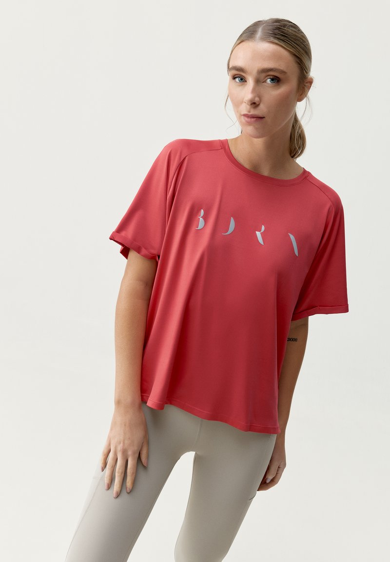 Červený sportovní top s krátkým rukávem a volným střihem, s stylizovaným šedým textem na přední straně. Hladká látka a kulatý výstřih.