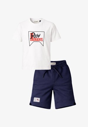 T-shirt bianca a maniche corte con logo "Roy Roger's" rosso e nero abbinata a pantaloncini blu navy con vita elasticizzata e toppa frontale.