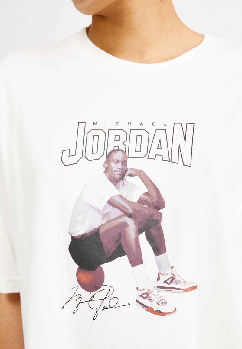 Camiseta de algodón blanca con un gráfico de una figura sentada al lado de un balón de baloncesto, con el texto "Michael Jordan" arriba y una firma debajo.