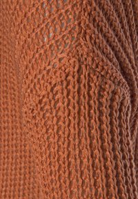 Gestricktes Baumwollkleidungsstück in rostorange, mit offener Webart, strukturiertem Finish und einem entspannten Design mit weiten Schulterauschnitten.