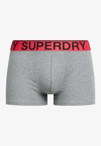 Boxers gris avec une ceinture rouge portant le nom de la marque "SUPERDRY" en lettres noires. Tissu doux et extensible avec un fit ajusté.