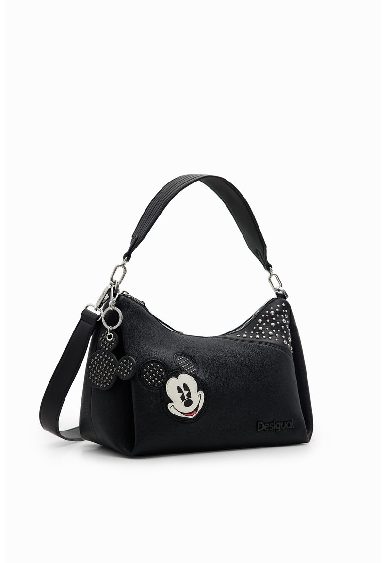 Sac à main noir avec un patch visage de Mickey Mouse, des détails cloutés, un petit porte-clés en forme de Mickey et une bandoulière amovible.