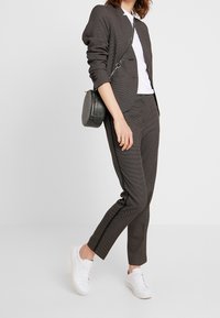 Blazer à carreaux gris foncé ajusté avec un pantalon assorti. Porté sur une chemise blanche et associé à des baskets blanches et un sac rond.