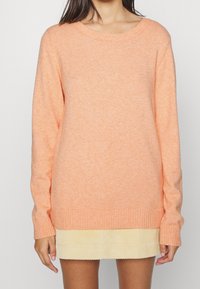 Suéter de punto en melocotón claro con un dobladillo y puños acanalados. Cuello redondo y mangas largas, con un acabado suave y ligeramente texturizado.