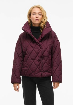 Burgundy quilted jacket with a high collar, drawstring waist, and snap closures. Features diamond-shaped stitching and side pocket.