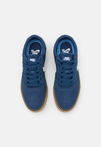 Nike SB -kengissä on tummansininen mokkanahkainen päällinen, sävyyn sopivat nauhat, vaaleansininen sisäpinta ja kumipohjat. Valkoiset logokoristeet.