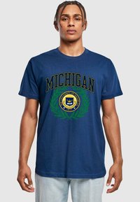 Jūrinio stiliaus medvilninis marškinėliai, kurioje užrašyta "MICHIGAN" auksinėmis raidėmis, aplink kurią yra apvalus universiteto emblema, išdėstyta žaliosios laurų šakos. Trumpomis rankovėmis, atsipalaidavęs siluetas.