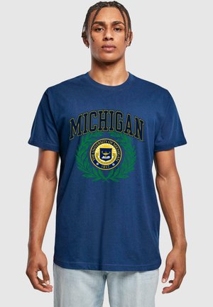 Navy modrá bavlněná trička s nápisem "MICHIGAN" ve zlatém písmu, kulatým univerzitním emblémem obklopeným zelenými vavřínovými listy. Krátké rukávy, uvolněný střih.
