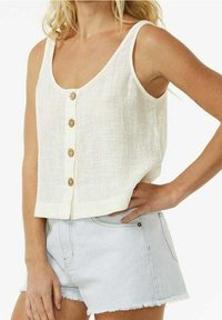 Crop top en lin blanc avec un col en V, doté d'une fermeture à boutons sur le devant et d'une coupe décontractée. Associé à un short en jean bleu clair.