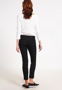 Černé vzorované slim-fit kalhoty s jemným designem, v kombinaci s bílým topem s dlouhým rukávem a černými slip-on botami, viděné ze zadní strany.