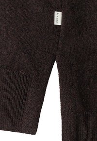 Pull en tricot marron avec une finition texturée, comportant une fente sur le côté et une petite étiquette de marque. Matière douce avec des poignets côtelés.