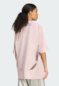 Top atlético rosa con mangas cortas, con acentos de lentejuelas en los laterales, cuello redondo y una textura de tela suave.